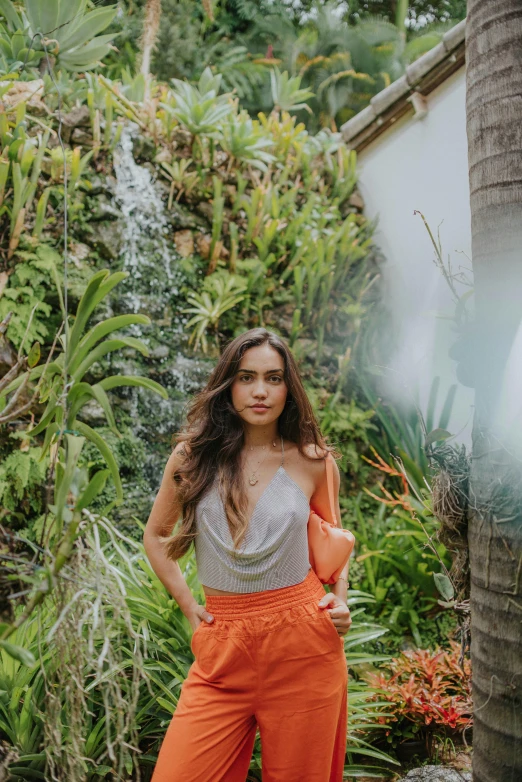 young woman in orange wide legged pants holding an umbrella in a tropical scene