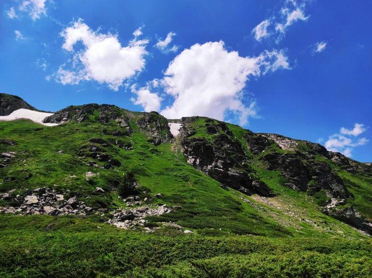 a green hill with a cloudy blue sky above