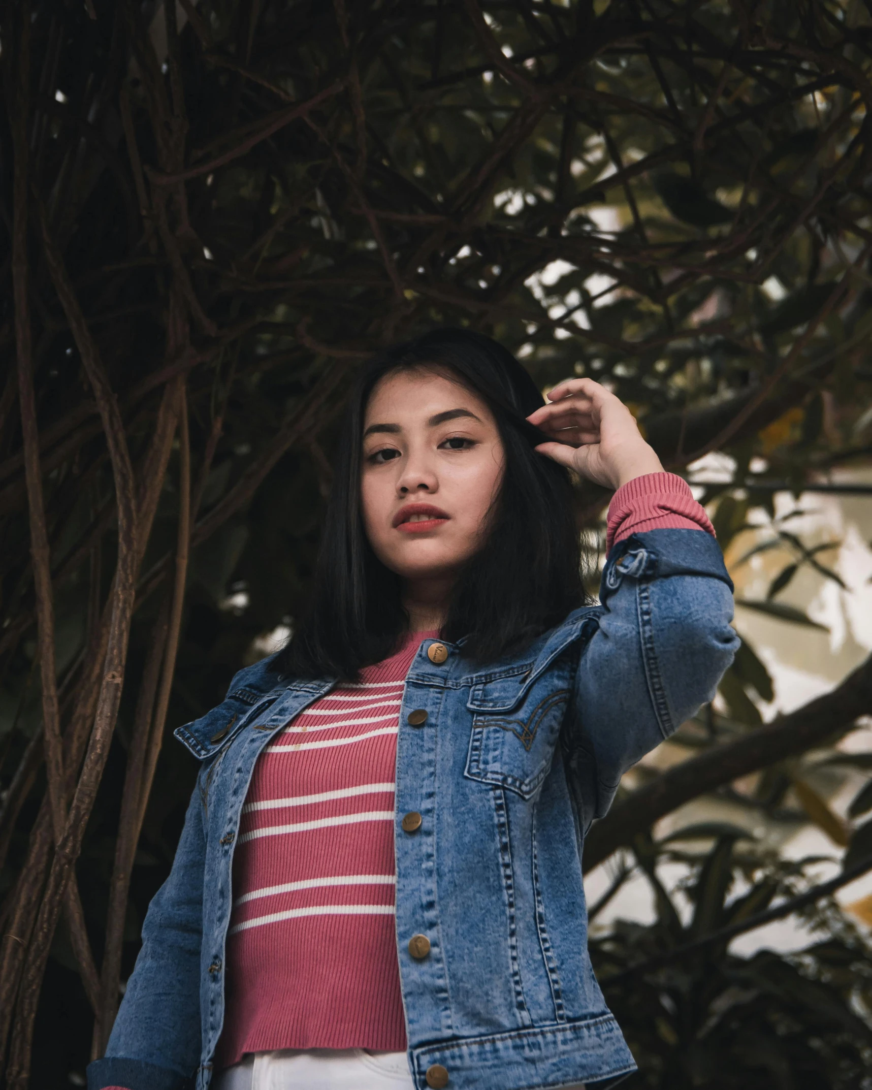 a woman stands in front of a tree and is wearing a jean jacket