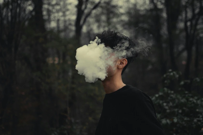 man standing in the woods, smoking an ash cigarette