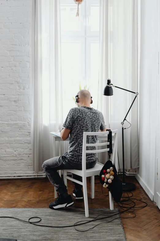 man in grey shirt sitting on a chair in front of window