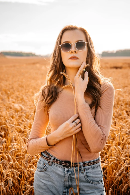 a girl standing in a wheatfield wearing sunglasses