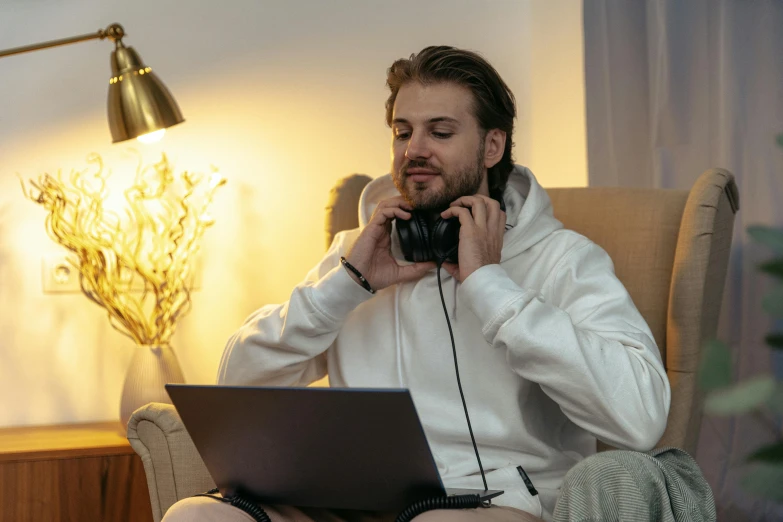 a man sitting in a chair talking on a cell phone with a laptop and a lamp behind him