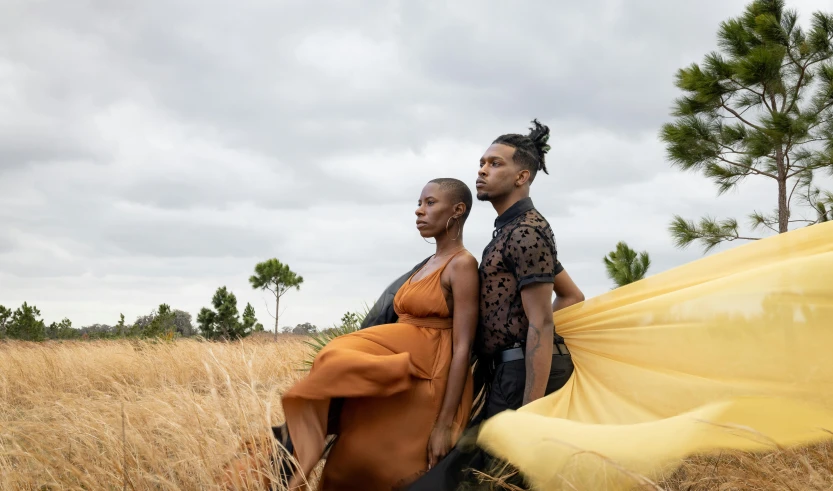 two young people standing by some dry grass