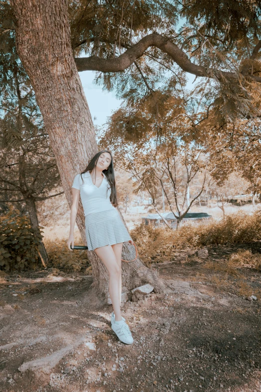 woman posing under a tree in a field near the woods