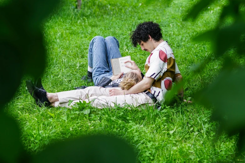 man reading a book with his companion while sitting on the grass