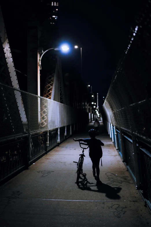 a man with his bicycle waiting to cross a night city bridge