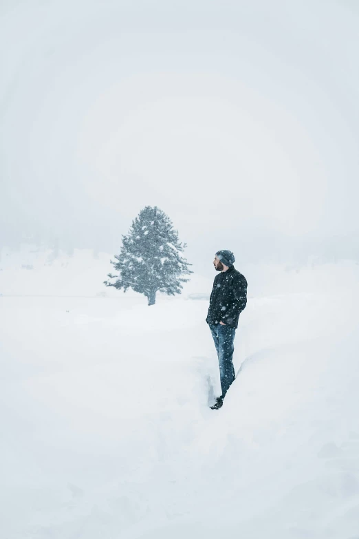 a man walking through deep snow in front of a lone tree