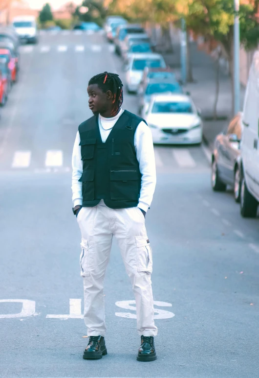 man wearing a black vest standing in street next to parked cars