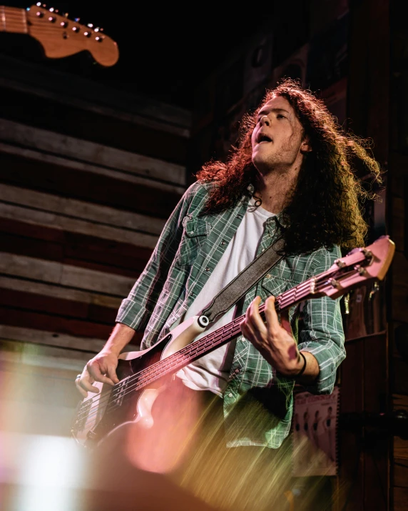 a young man with long hair playing a pink guitar