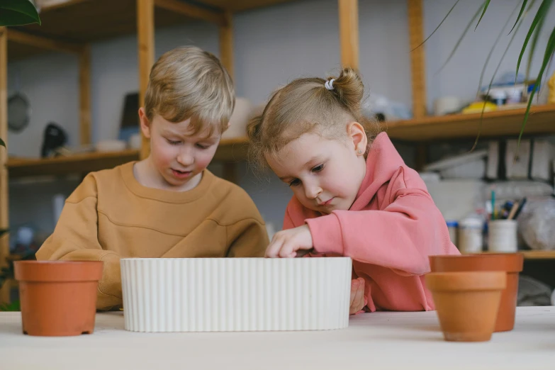 two children are playing with small pots and sand