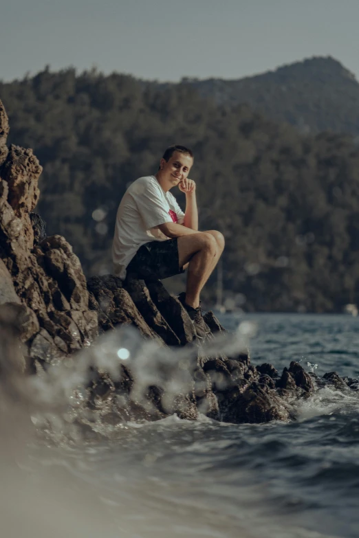 man sitting on rock near ocean and mountains