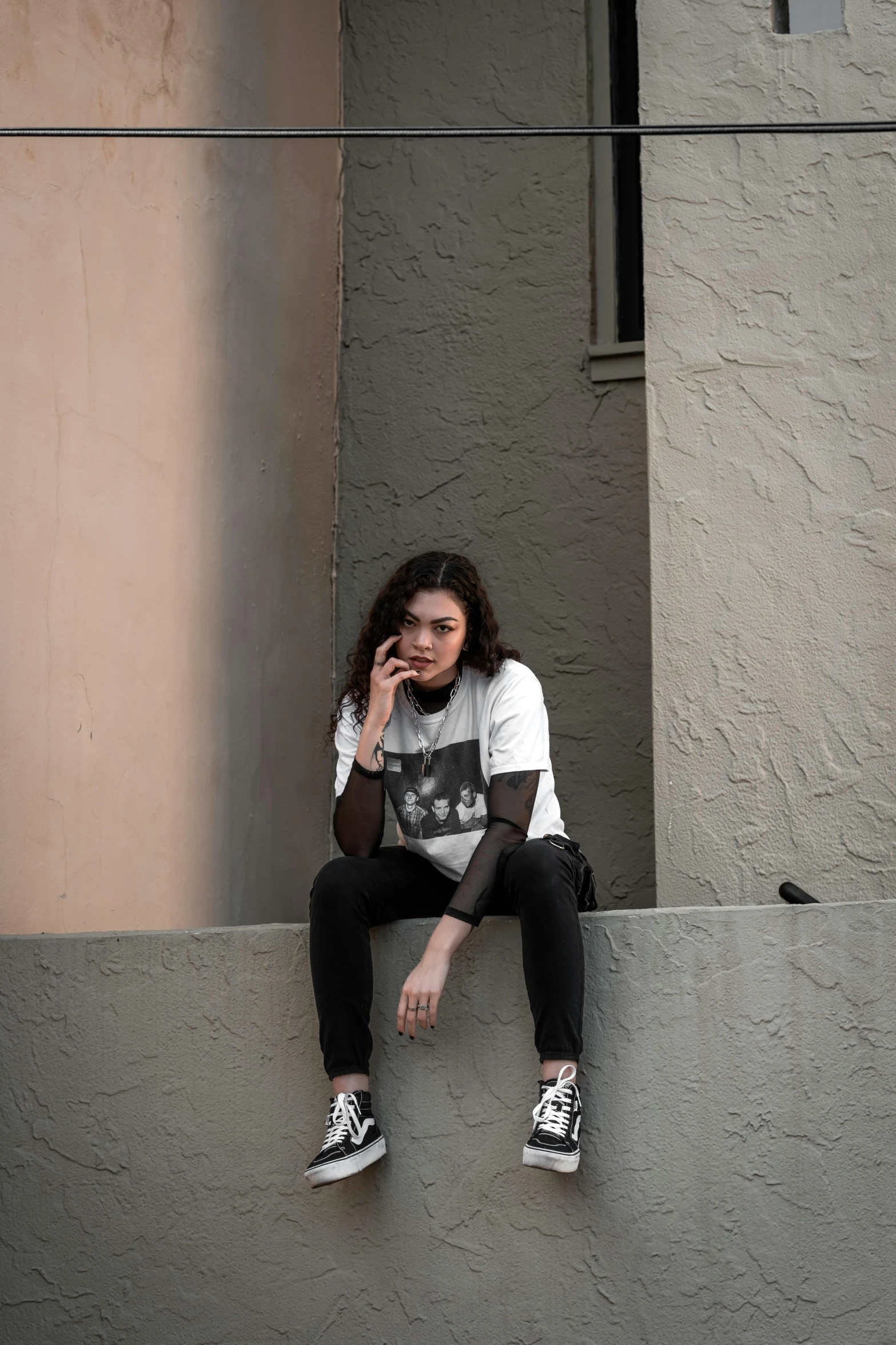 a woman in a white shirt and black jeans sitting on stairs talking on her cell phone
