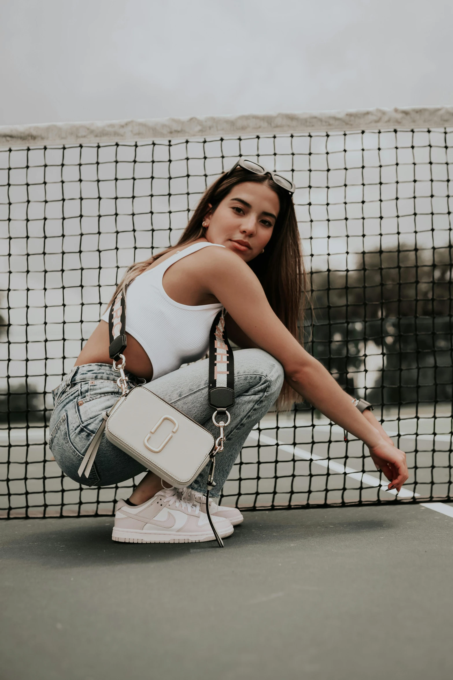 a woman holding a purse crouches on a tennis court