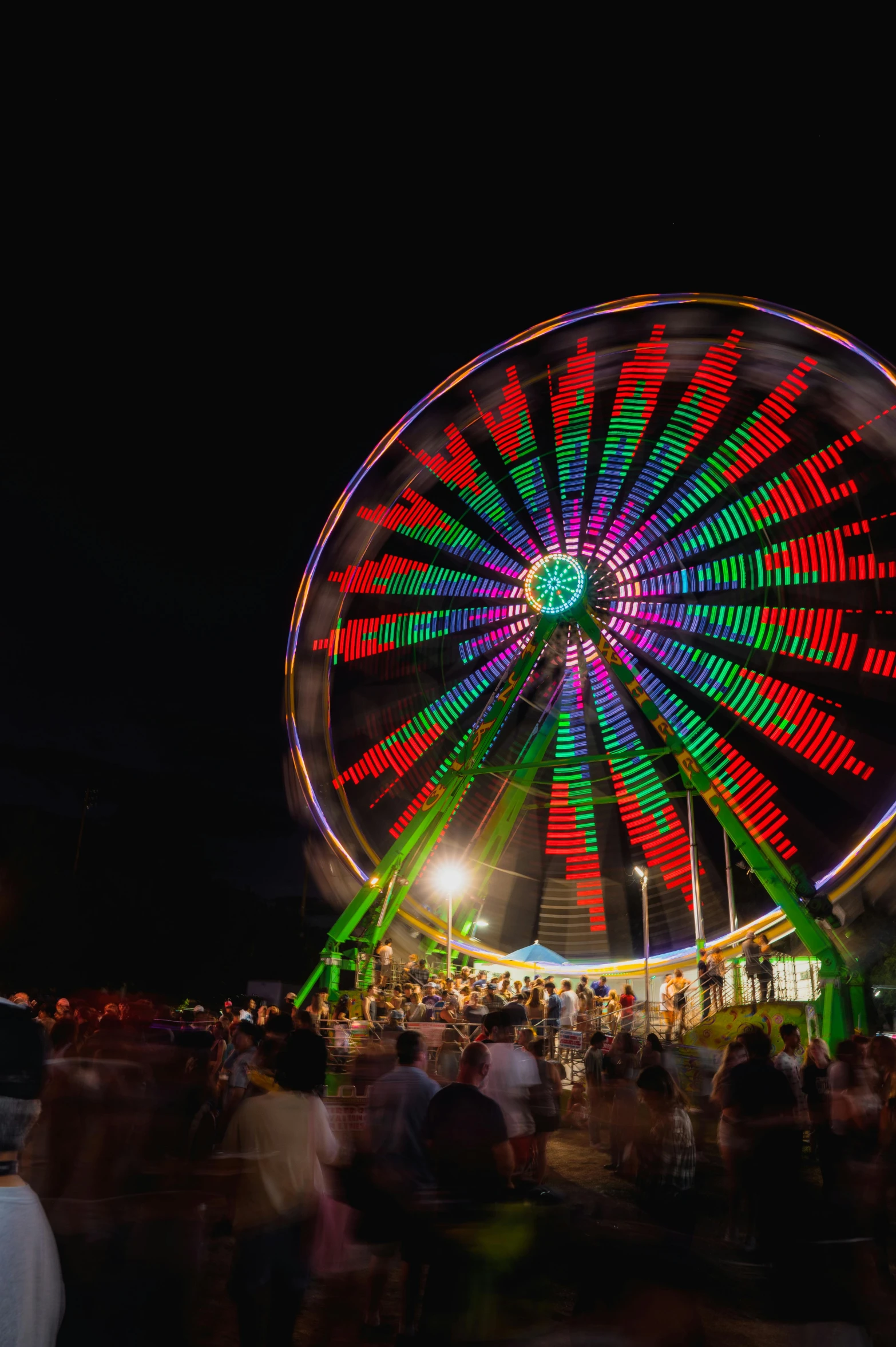 a colorful wheel on a dark evening with people milling around