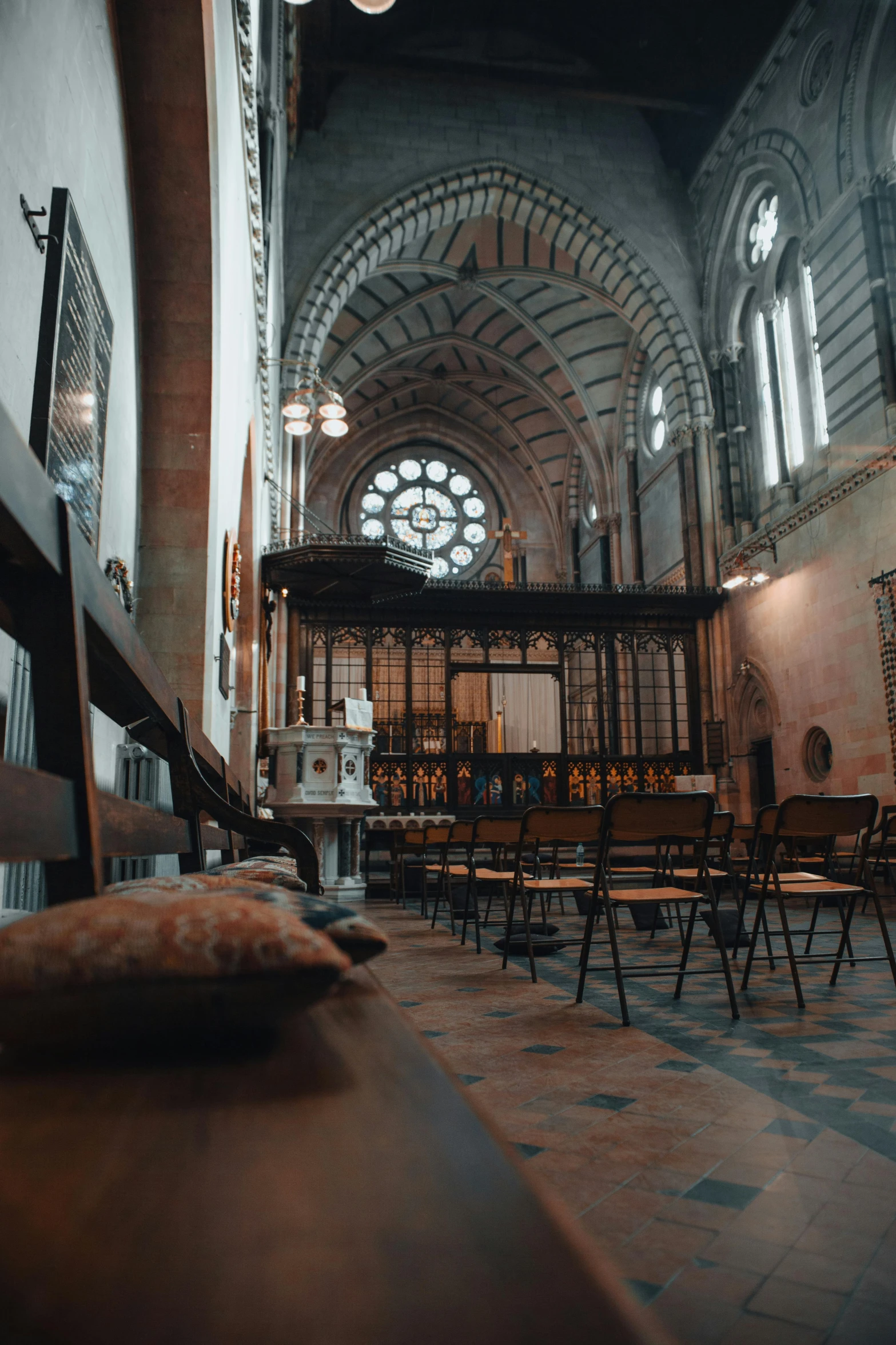 an old, well - lit, dirty church with pews and chairs in front of stained glass windows