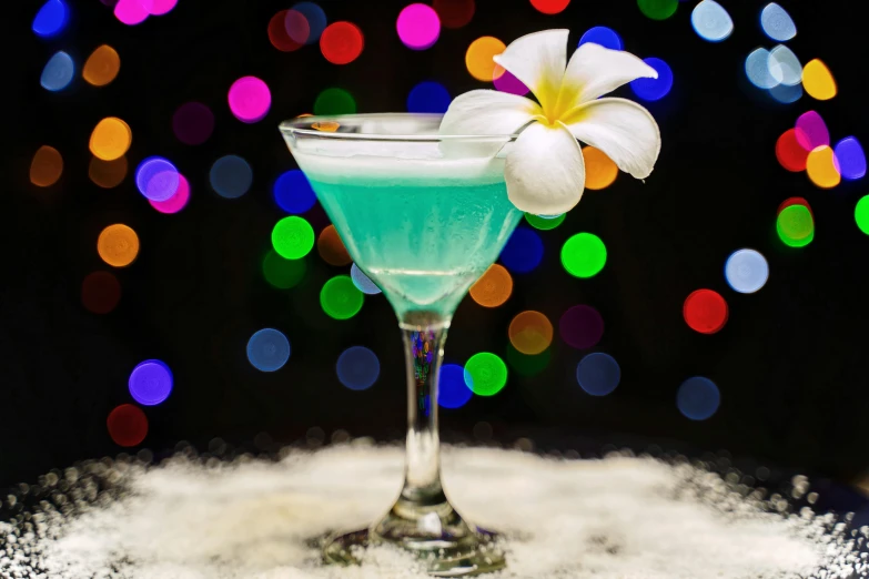 a blue martini is sitting on a table in front of multi - colored lights