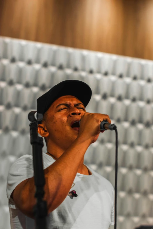 man singing into a microphone while standing by a wall