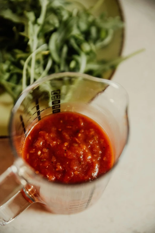 a glass measuring cup filled with sauce sitting on top of a table