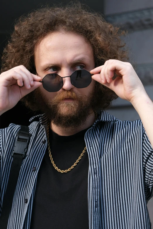 a man wearing a striped shirt holds up two pair of glasses over his eye