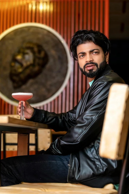 man with beard and leather jacket sitting in front of art display