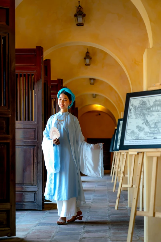 a woman in a blue outfit stands in an archway with her arms folded