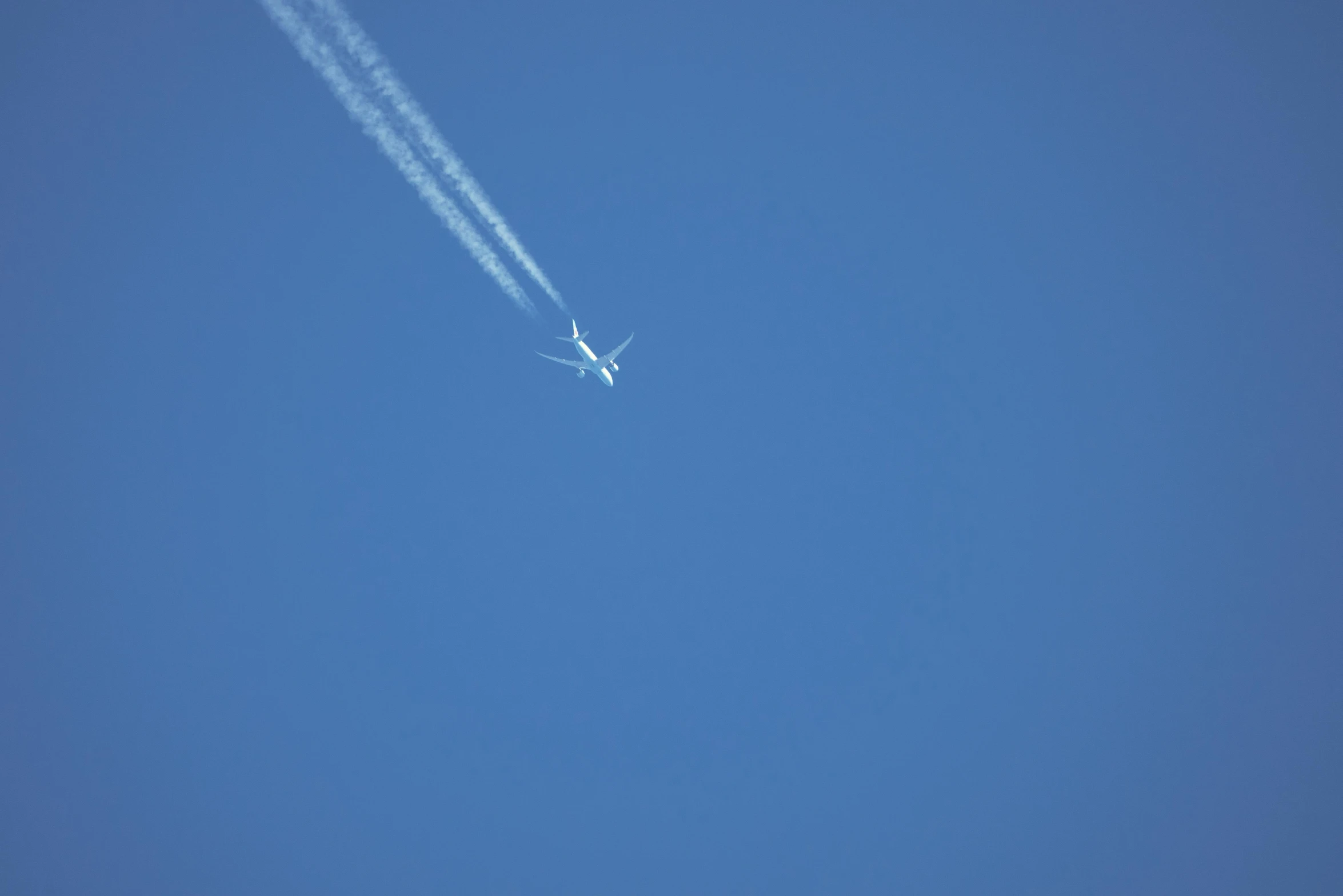 a plane flying high in the sky with a contrail trailing from it's back