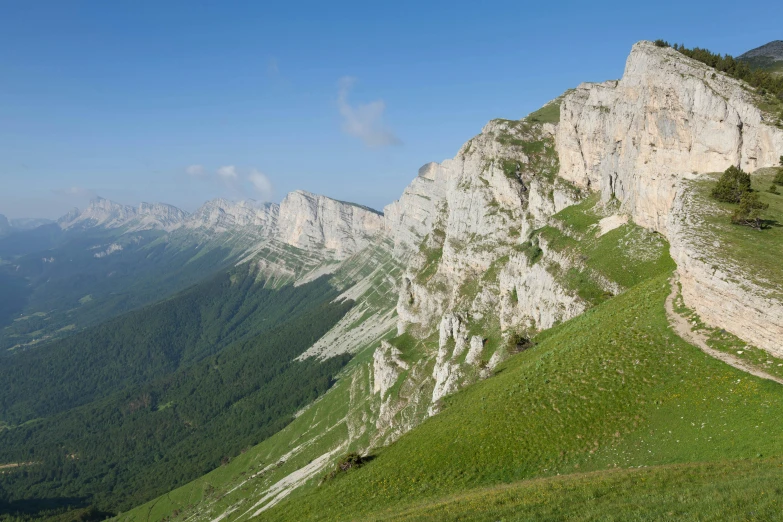 a man walking up a green steep slope next to a tall mountain