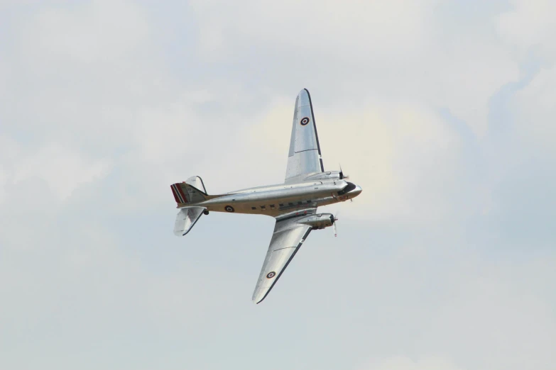 a silver airplane flying across a cloudy sky