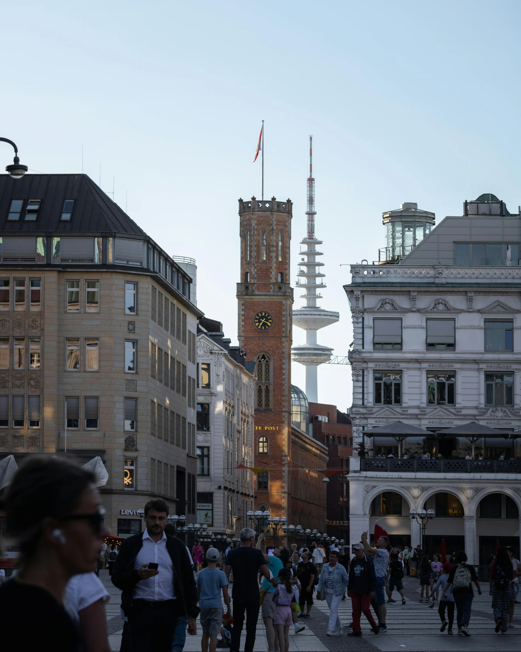 an outdoor clock tower sits above the street as pedestrians walk on the sidewalks