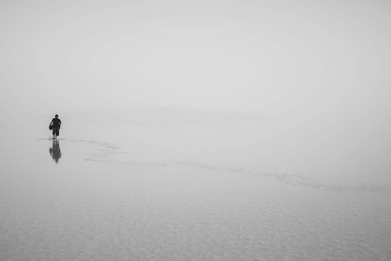 a lone person walks through the fog of an empty beach