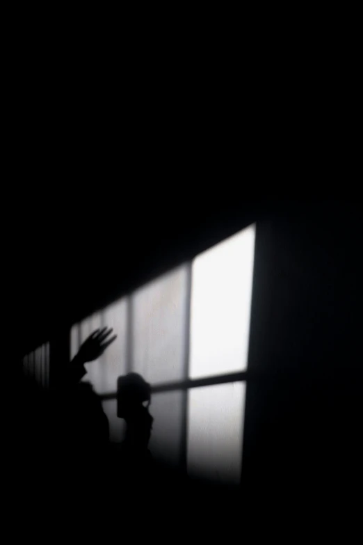 silhouette of a person near a window with their hand up and their arm in the air