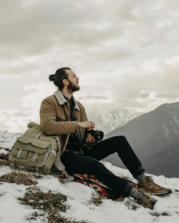 a bearded man with a backpack sitting in the snow