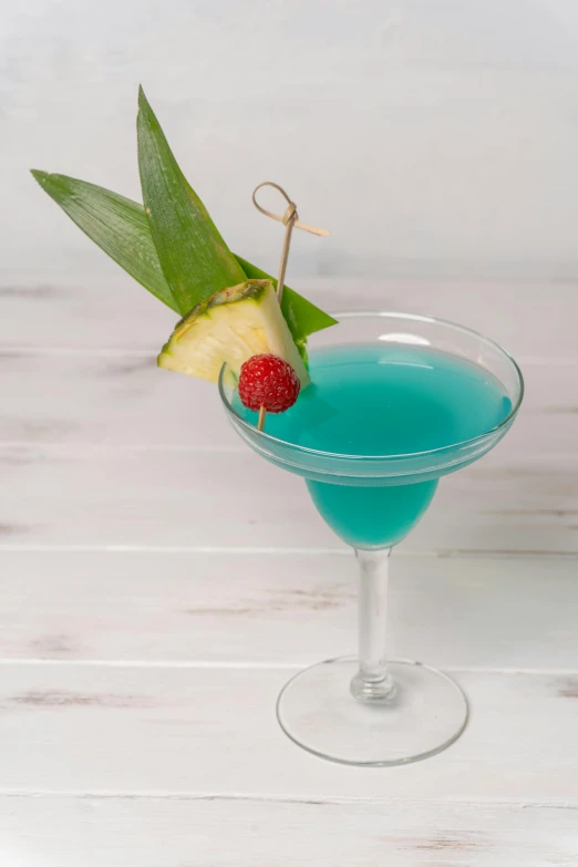 a small blue cocktail in a glass with a piece of apple and pineapple