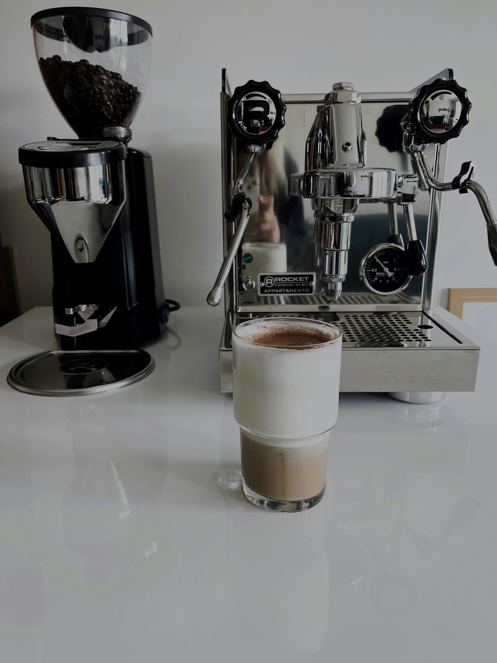 a glass of coffee and espresso machine with a mirror on the wall