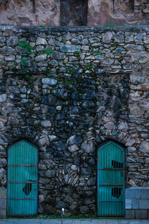 two green doors on a stone building next to a red fire hydrant