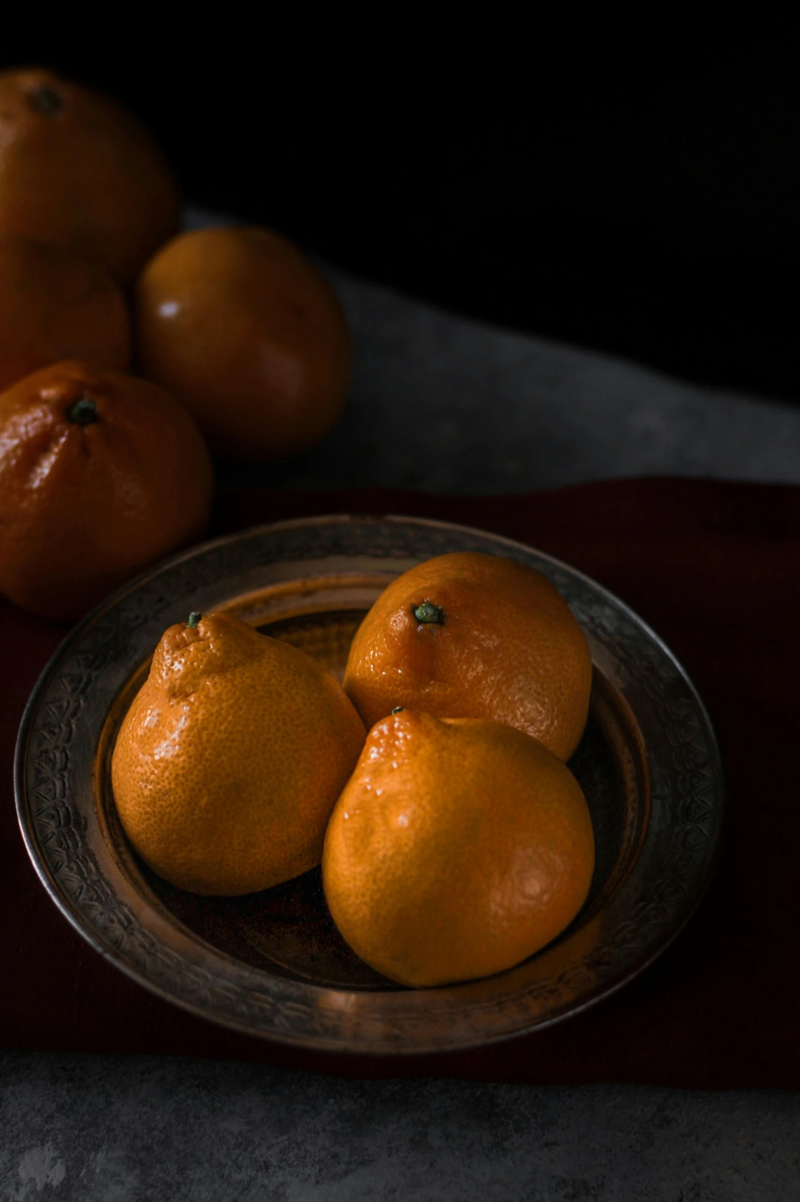 oranges in a bowl on a table, next to a group of tangerines