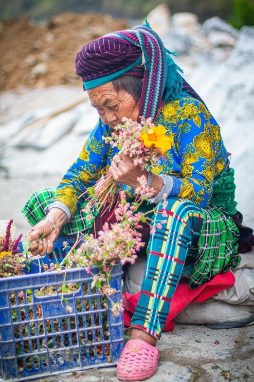 an old woman in brightly colored clothing placing flowers inside her basket