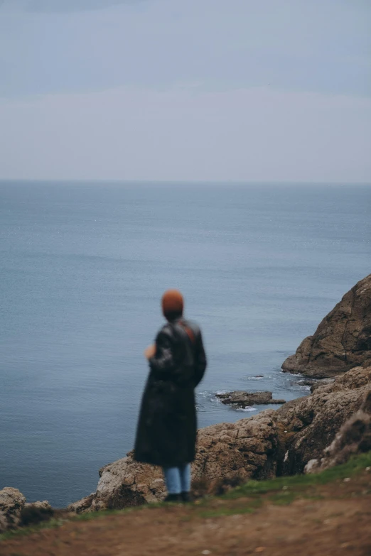 a person standing at the edge of a cliff on top of a hill overlooking a body of water