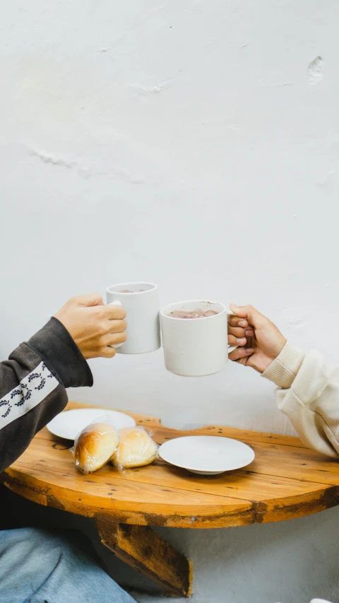 two people are toasting at a table with plates of bread and coffee