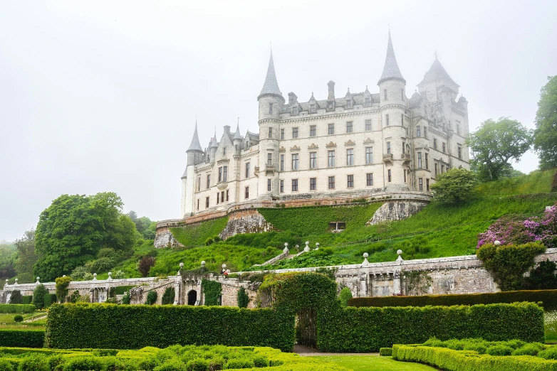 a stone castle on a hill above some hedges