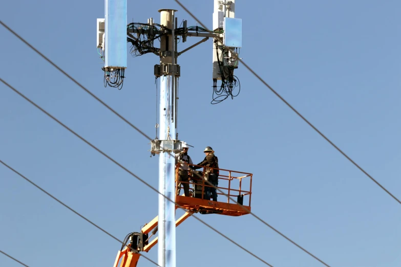 two men working on an antenna system under blue skies
