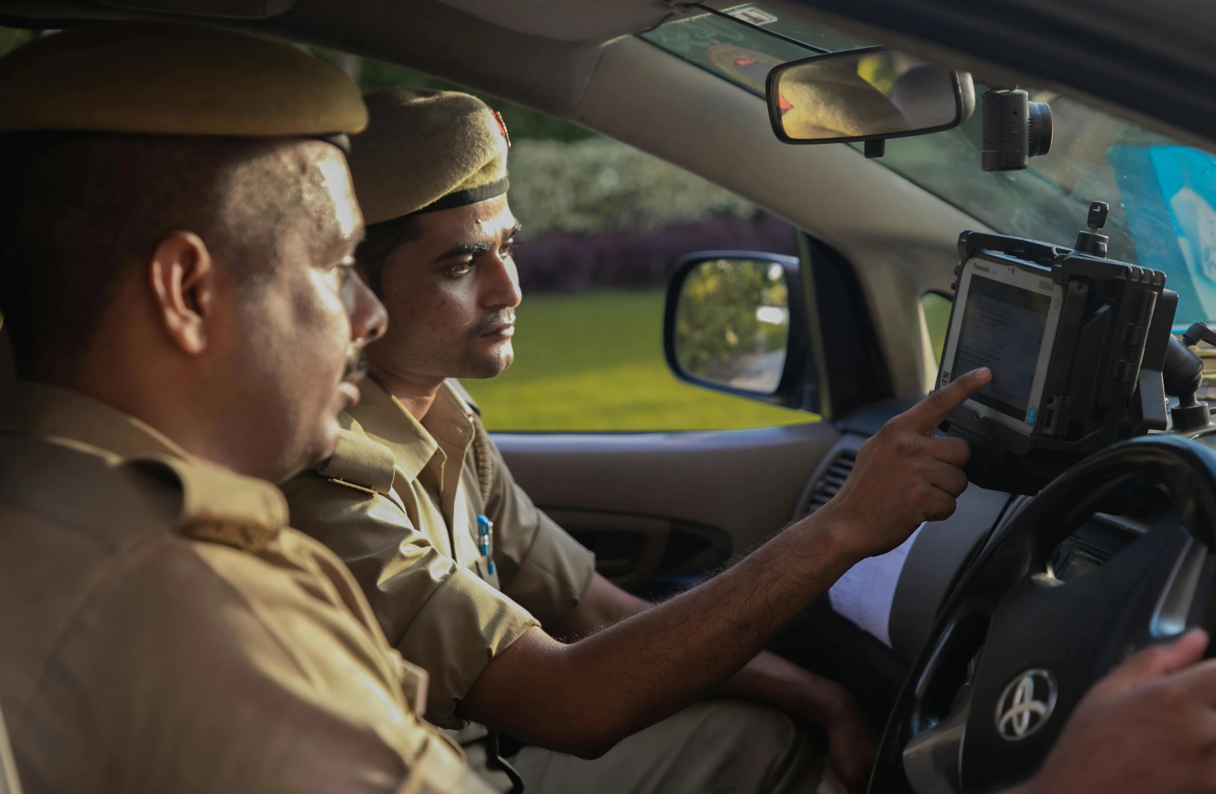 two men wearing uniforms driving a car and looking at soing on a camera