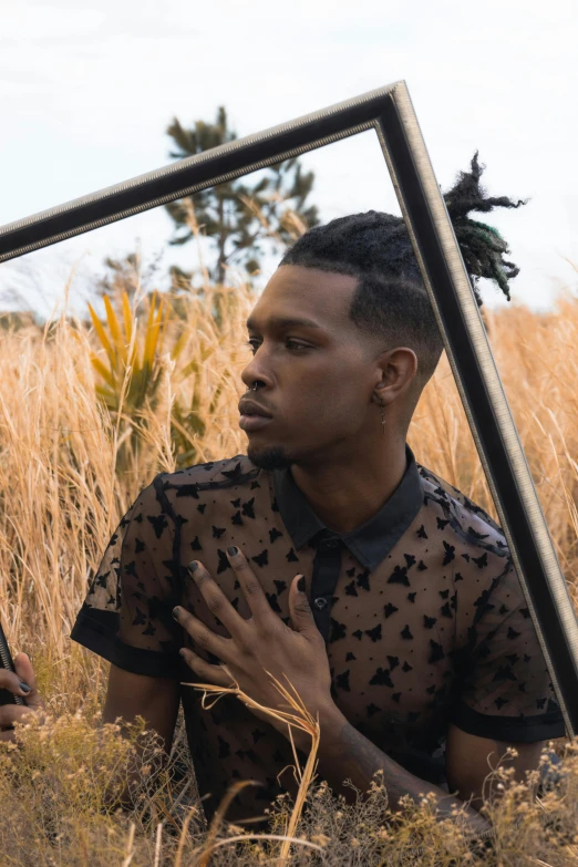 the man is sitting in the tall grass and has his hands clasped