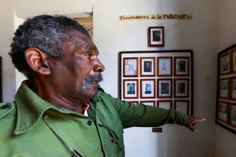 an old man is pointing to an array of family pictures on the wall