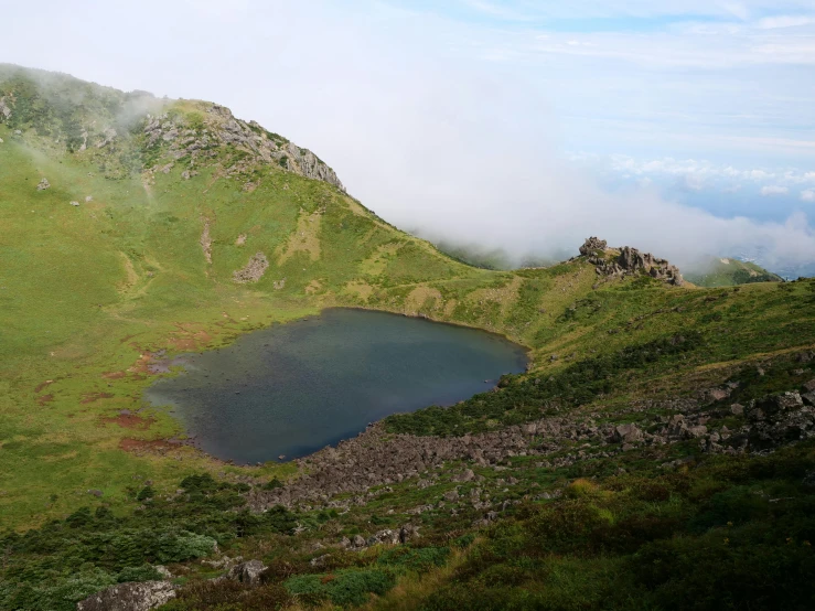 there is a small lake in the grass near a green mountain