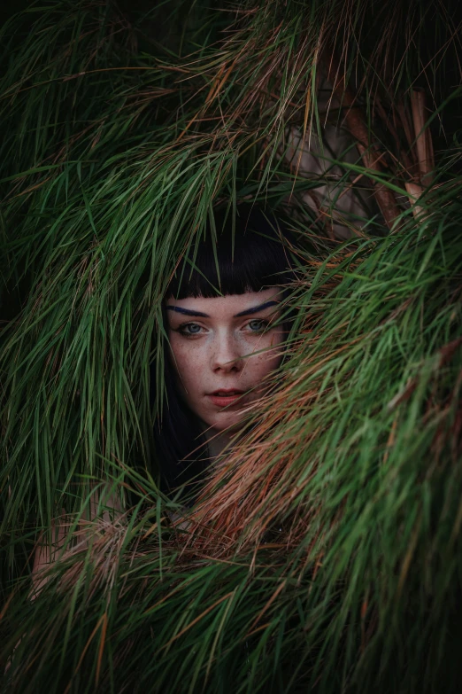 a woman hiding between grass nches in front of her