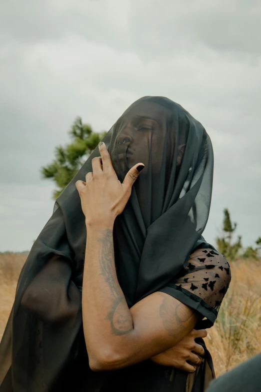 a woman in black dress covering her face with a large veil