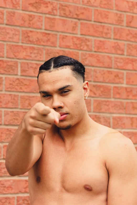 a shirtless man poses by a brick wall