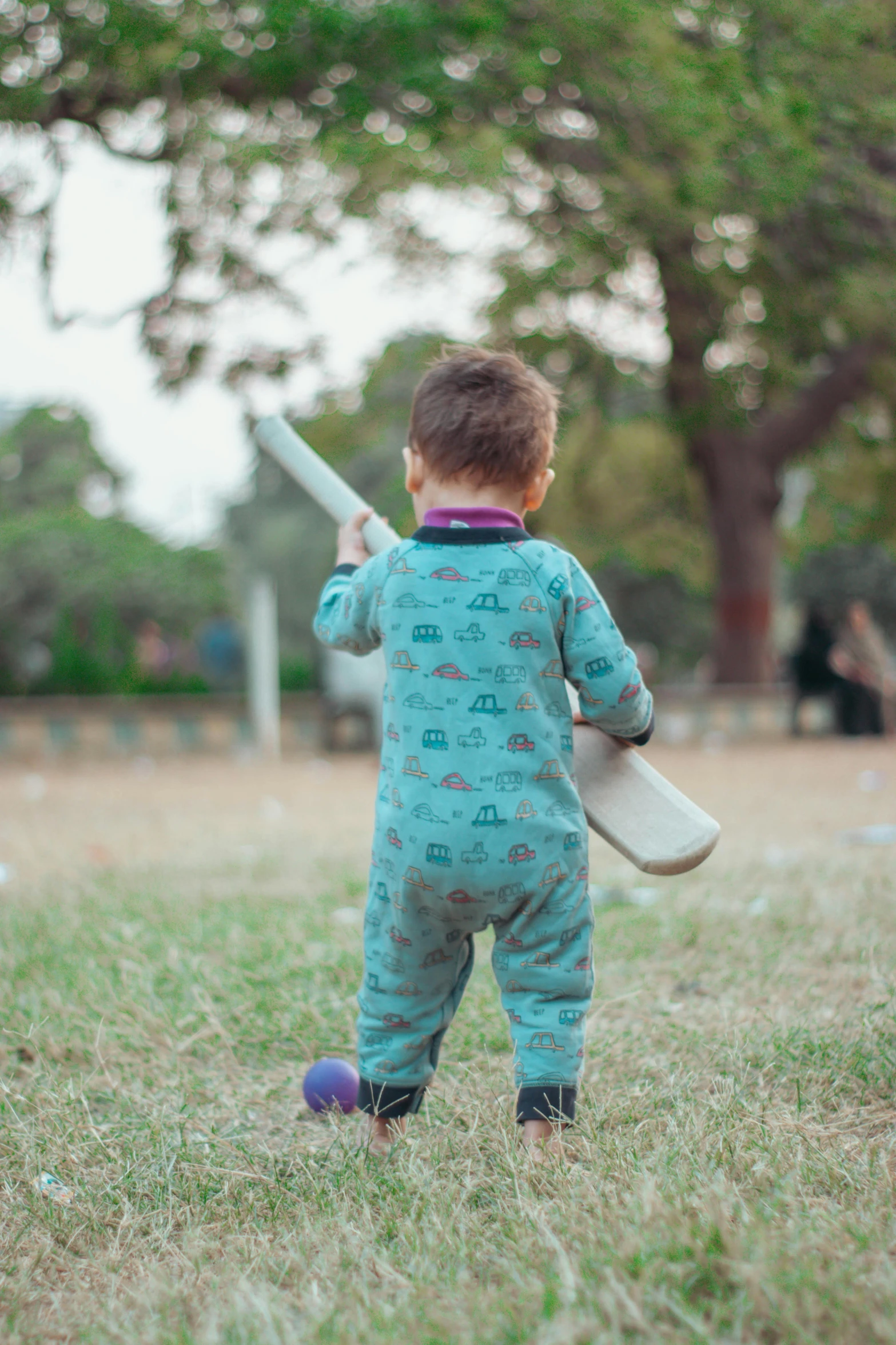 baby standing in a field playing with a ball and bat